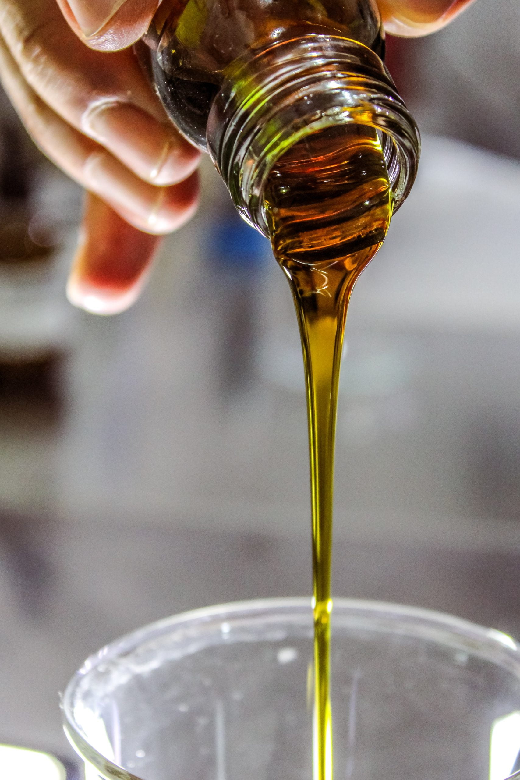 person holding clear drinking glass of coffee with olive oil liquid